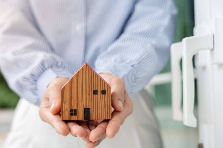 Une personne tient une maquette de maison en bois symbolisant la protection offerte par l'assurance habitation.