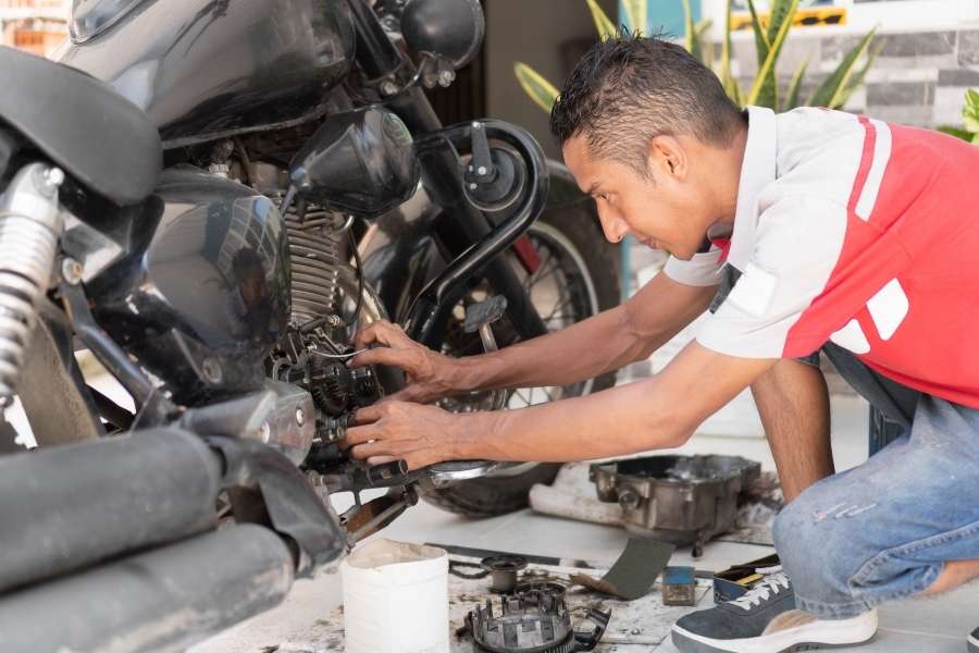 Un technicien réalise un entretien moto hivernal en travaillant sur le moteur d'une moto noire dans un atelier extérieur.