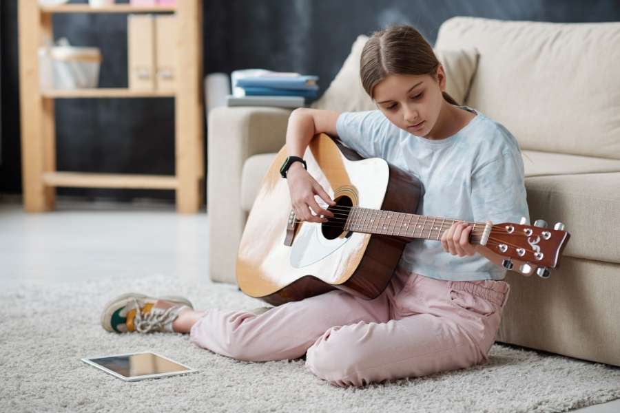 Jeune fille apprenant la guitare en autodidacte à domicile avec tablette numérique comme support pédagogique