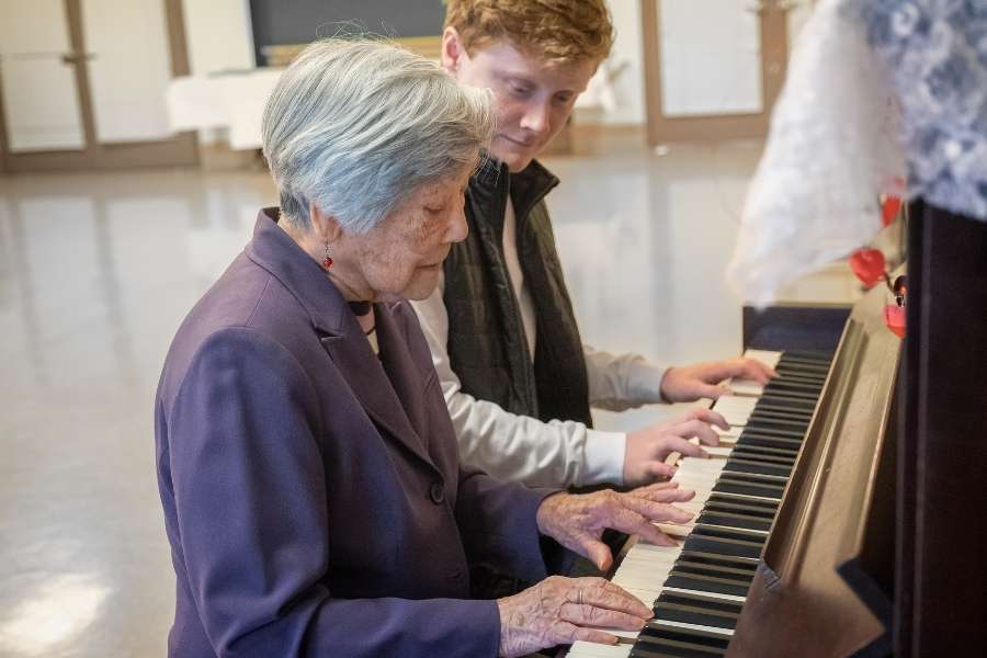 Une personne âgée joue du piano lors d'une séance de musicothérapie accompagnée d'un jeune accompagnant.