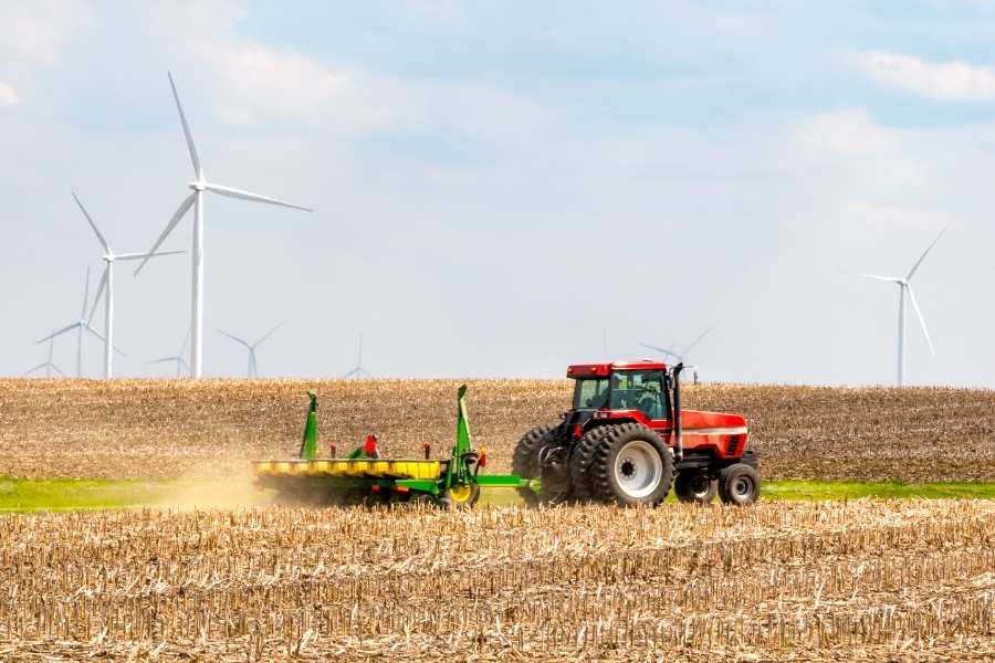 Un tracteur rouge travaille dans un champ agricole moderne avec des éoliennes en arrière-plan symbolisant l'agriculture urbaine durable.