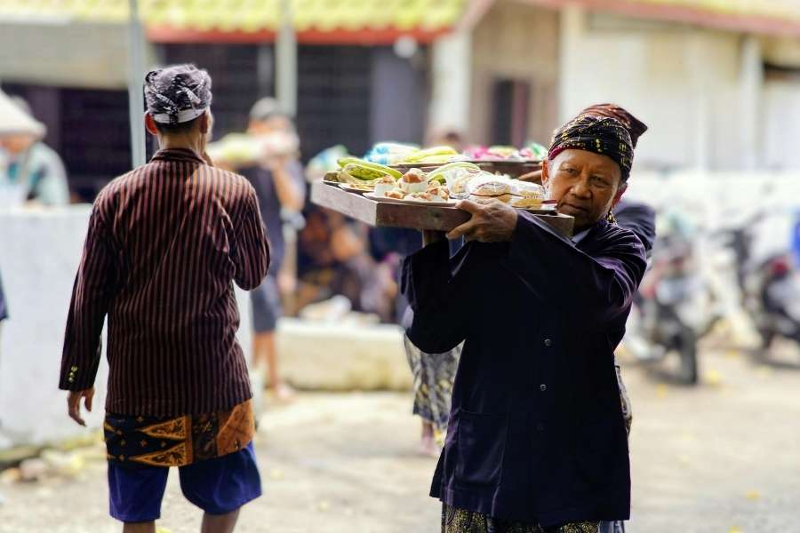 Un vendeur en tenue traditionnelle porte un plateau de produits frais sur un marché, reflet authentique de la cuisine locale.