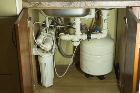 Une vue de l'intérieur d'un meuble de cuisine montrant un système de traitement de l'eau complet avec ses filtres et son réservoir de stockage.