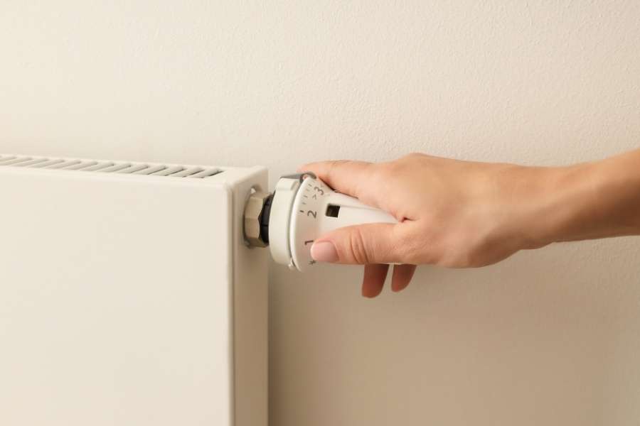 Une main ajuste le robinet thermostatique lorsque les radiateurs font du bruit.