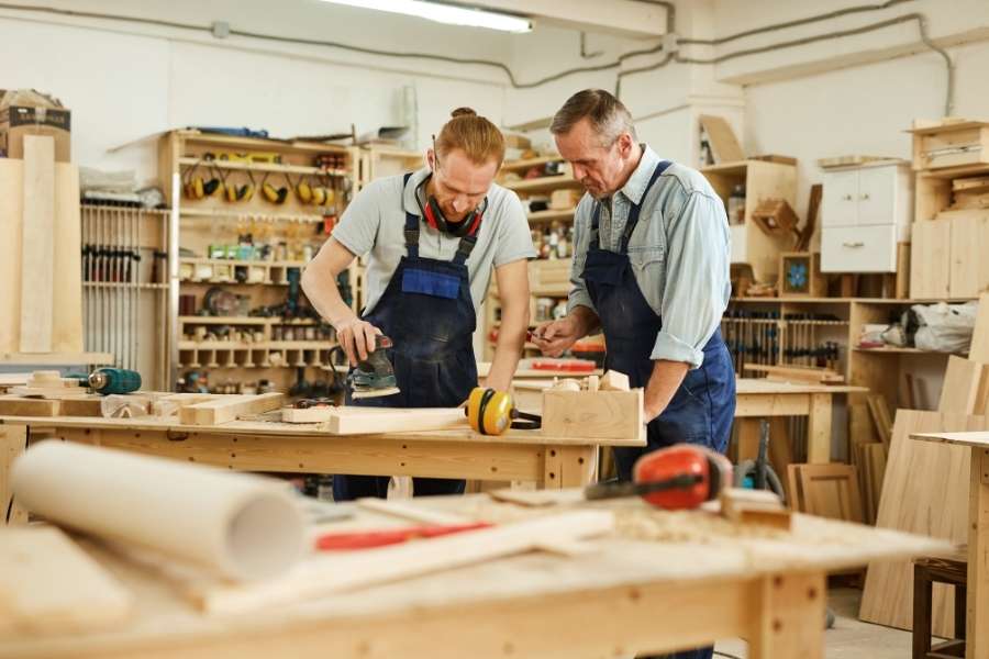 Deux artisans s'activent dans un atelier de menuiserie pour façonner du bois travaillé.